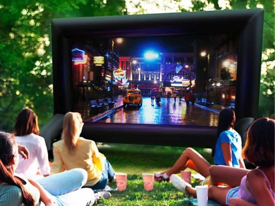 people sitting outside watching a movie on a large inflatable screen