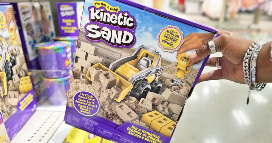 hand grabbing Kinetic Sand Dig & Demolish Playset from store shelf