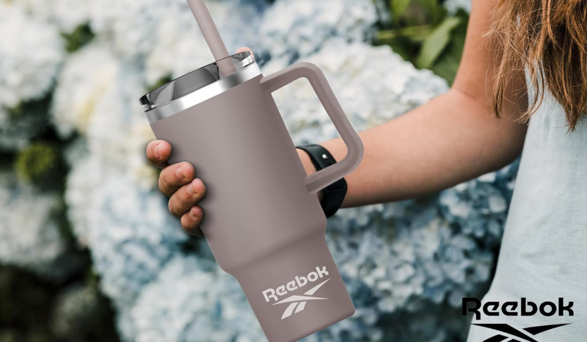 woman holding reebok gray tumbler in front of white flowers