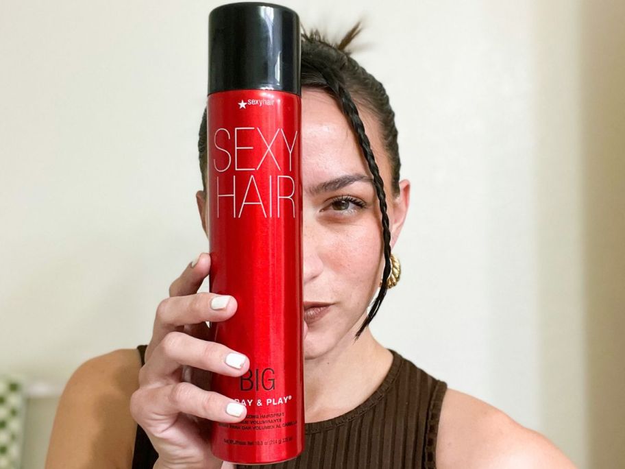 Woman holding a bottle of Sexy Hair Spray and Play Hairspray in front of her face