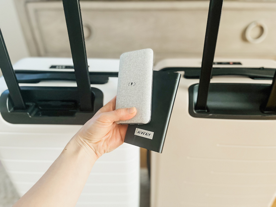 hand holding a gray battery pack with away battery pack in front of suitcases