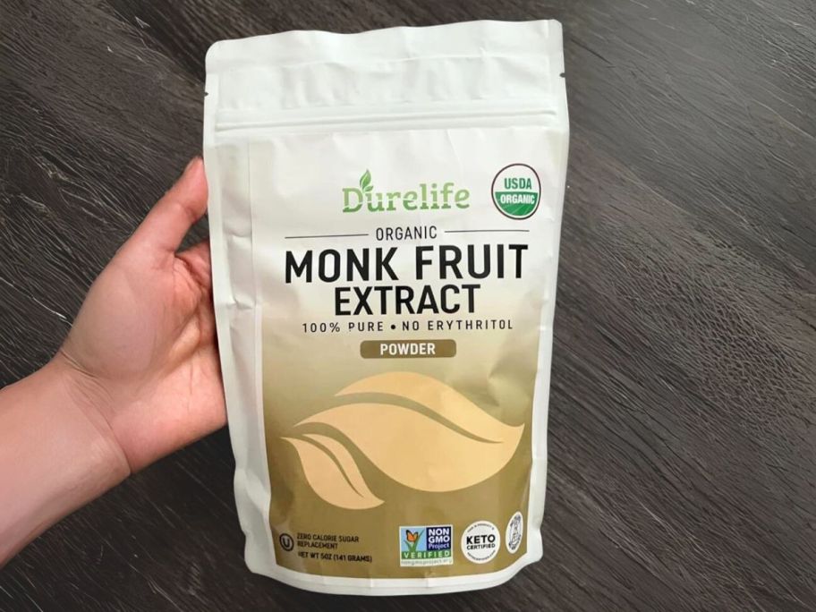 hand holding bag of durelife monk fruit extract over dark wooden floor