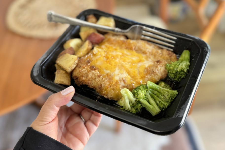 hand holding up cooked chicken and brocooli meal