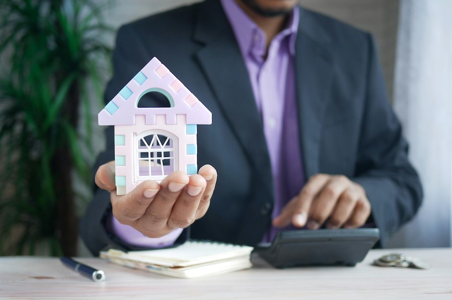 person typing on calculator holding up a toy house