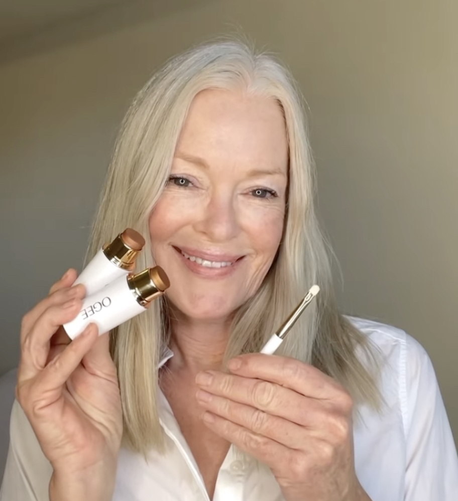 woman holding up ogee makeup stick with brush smiling