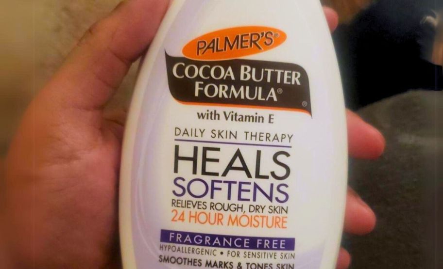  a woman's hand holding a bottle of palmers unscented cocoa butter lotion 