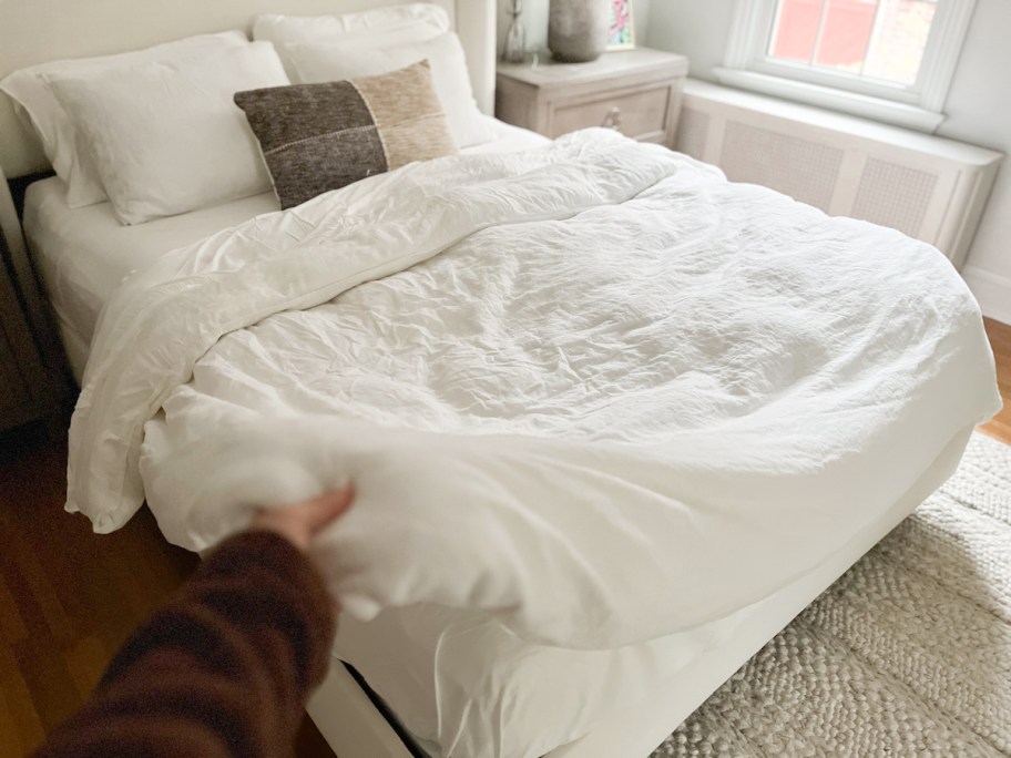 hand holding corner of white duvet on bed with pillows