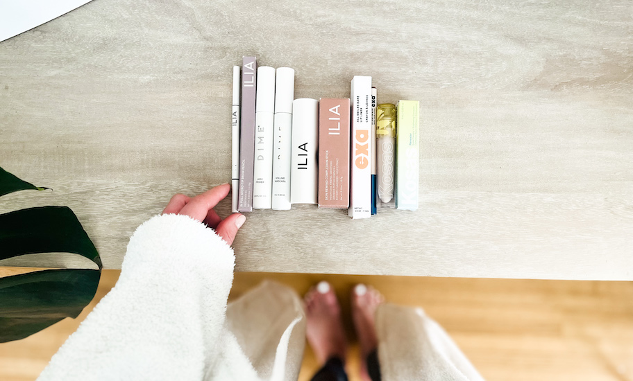 hand holding ILIA eyebrow pencil on wood table with other cosmetics in a row