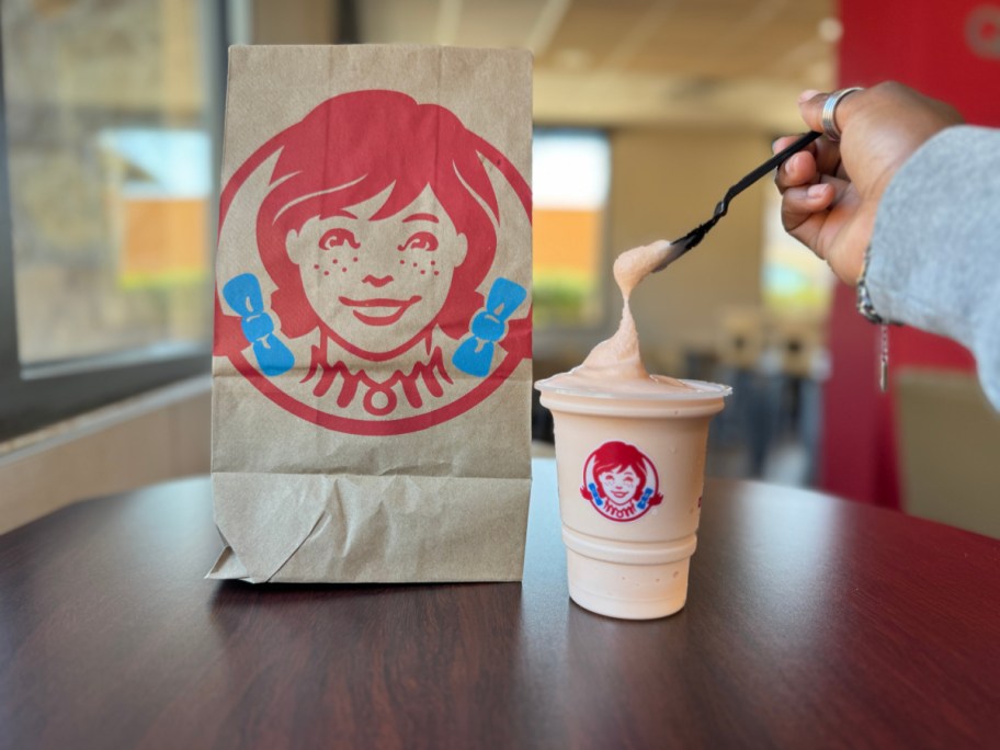 hand dipping a spoon into an orange dreamsicle wendys frosty inside the restaurant