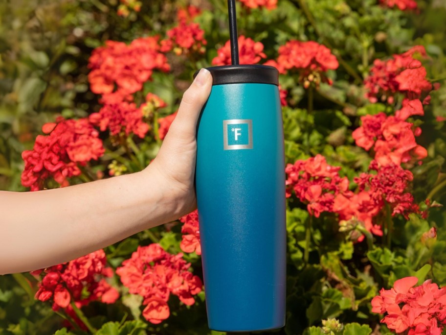 hand holding a blue ombre Iron Flask tumbler with pink/orange flowers behind it