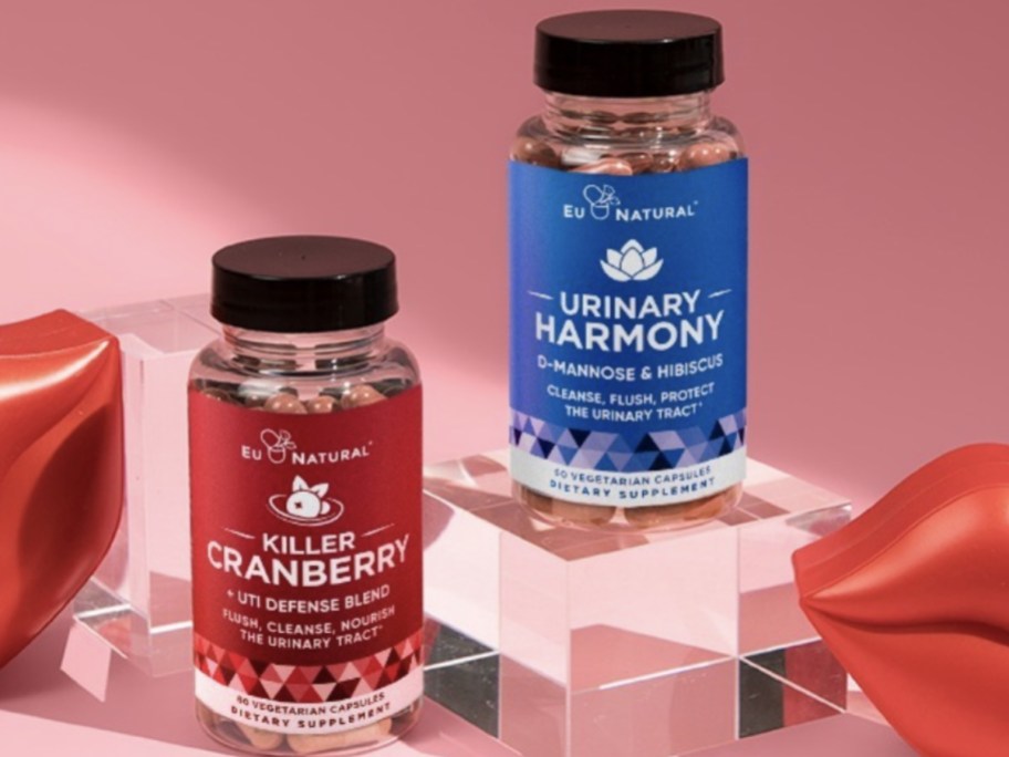bottles of EU Natural Killer Cranberry and Urinary Harmony supplements on a pink background