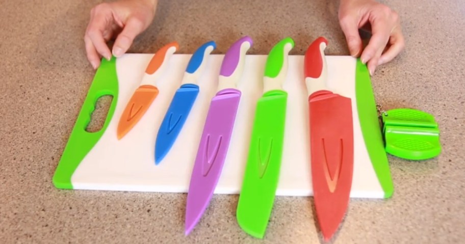 cutting board with colorful knives and knife sharpener on a counter