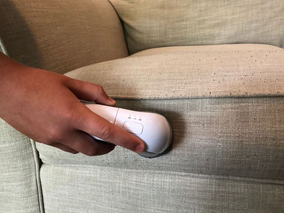 A couch cushion is shown with pilling as a woman is using a fabric shaver on it. 