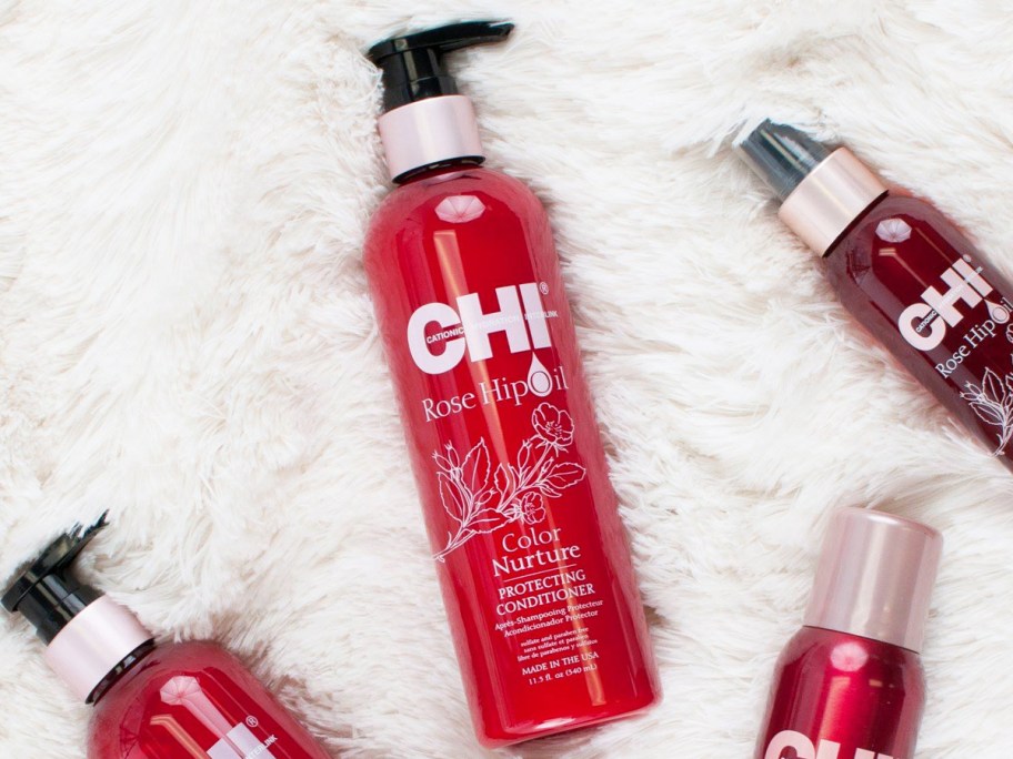 red bottle of CHI Rosehip Oil Conditioner near other products on a white fuzzy blanket