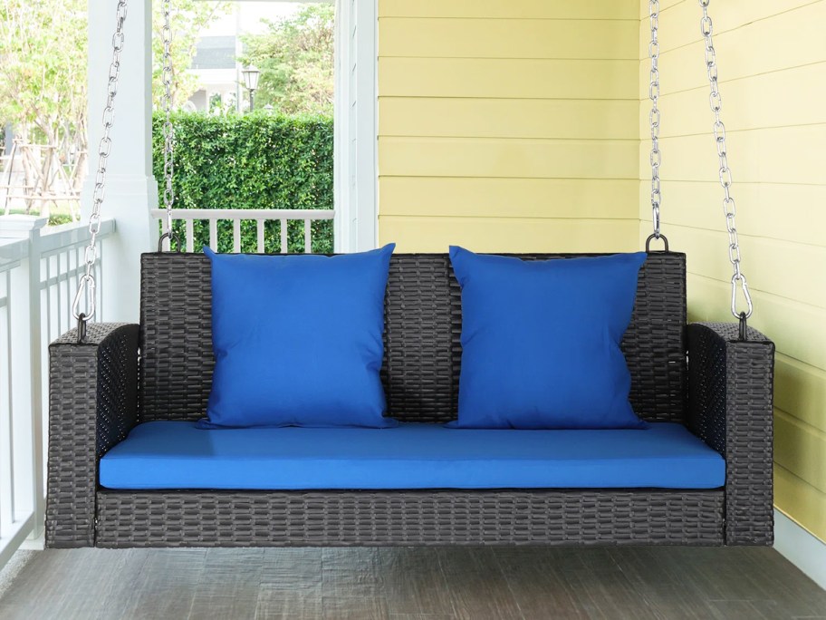 brown wicker porch swing with blue cushions and pillows