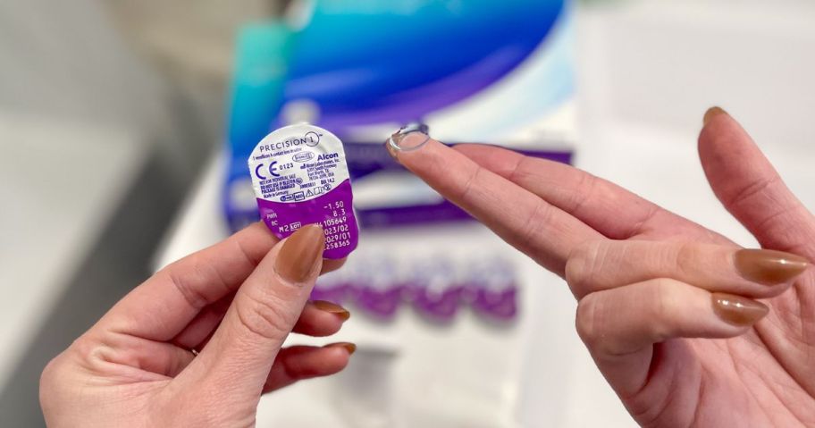 Hand holding a pack of disposable contact lenses in the left hand and a contact on the middle finger of the right hand