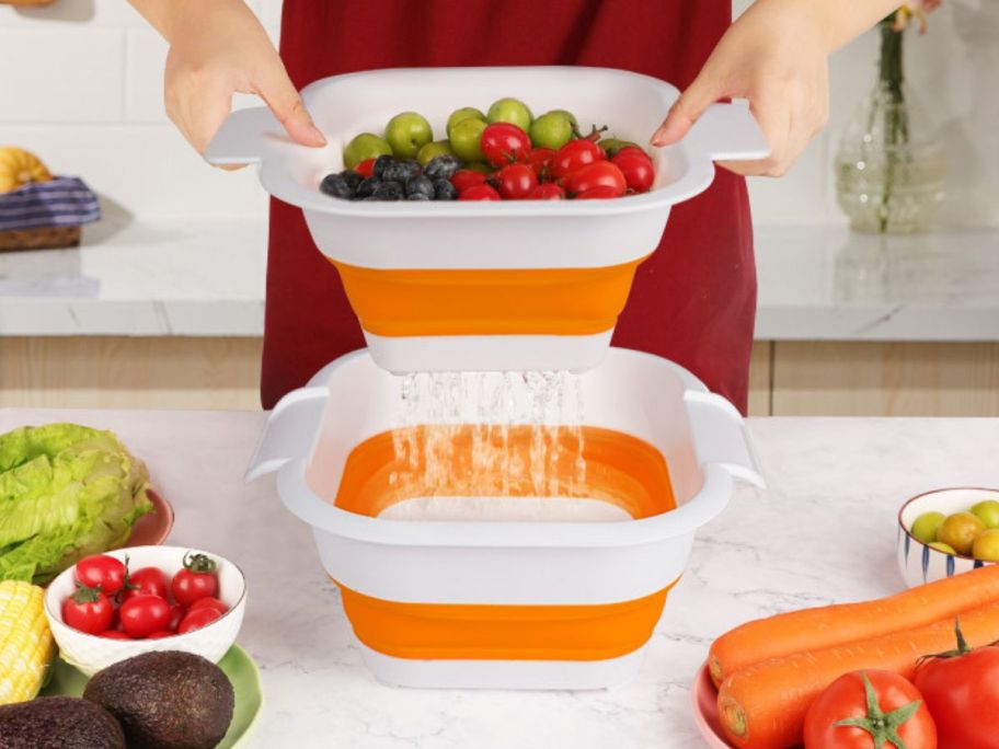A woman lifting up an orange collapsible strainer with fruit and veggies inside 