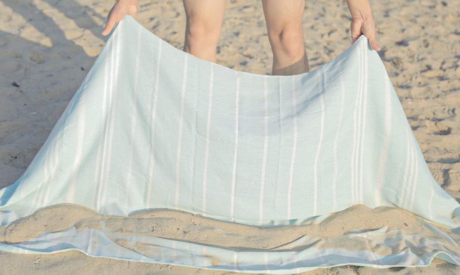 person picking up a Turkish Beach Towel up from sand with sand rolling off it