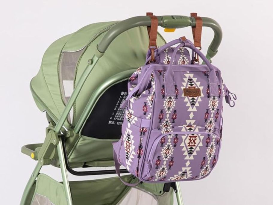 purple patterned Wrangler diaper bag backpack hanging on stroller handle