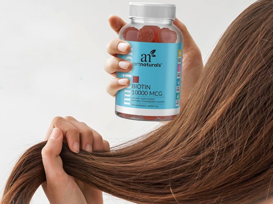 girl holding biotin gummies bottle and holding part of her hair