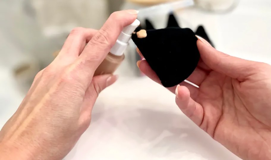 hand holding a black makeup puff and applying liquid foundation