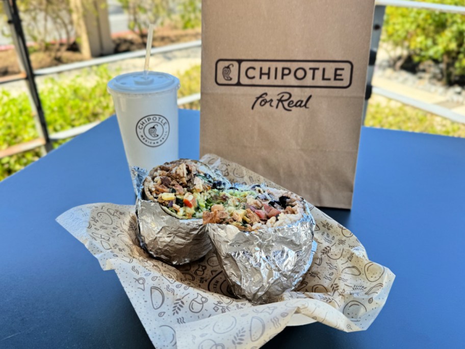 chipotle burrito displayed in front of a to-go bag and drink cup