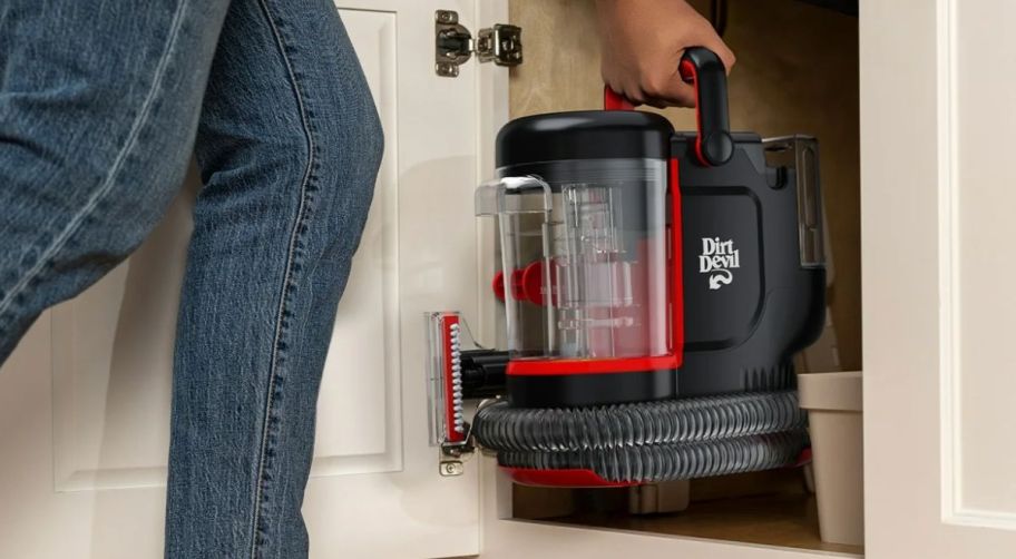 a woman tashing a dirt devil portable spot cleaner under a kitchen sink