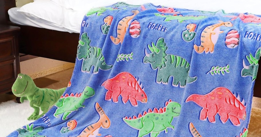 blue plush blanket with colorful dinosaurs spread out over blanket, stuffed Dino on floor beside it