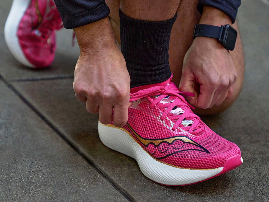person tying pink saucony shoes on feet