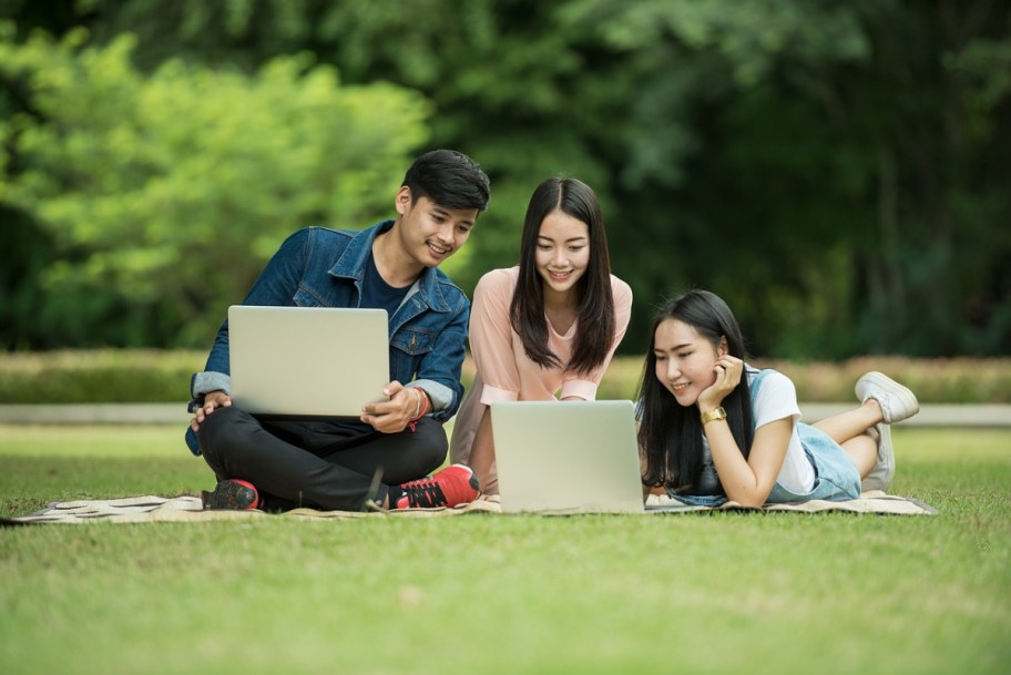 a group of students studying outside on computers, perhaps applying to college scholarships for high school students