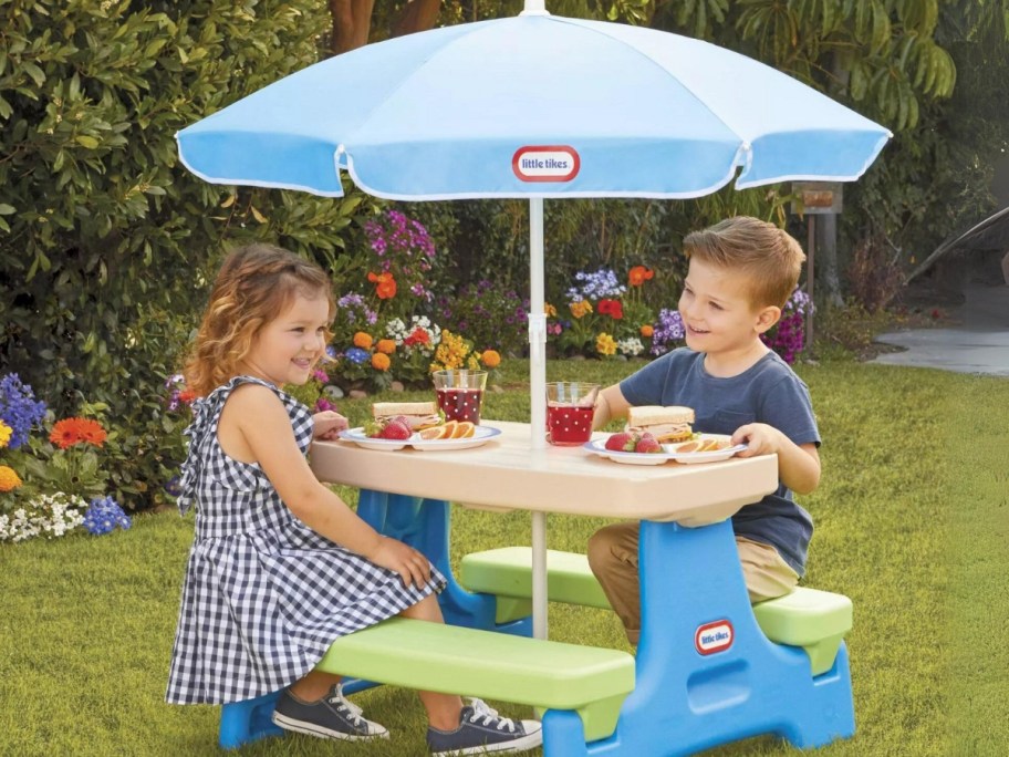 toddler boy and girl sitting at a Little Tikes picnic table with a blue umbrella