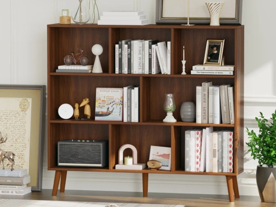 large, dark brown mid century modern style small bookcase with lighter color legs filled with books and knick knacks