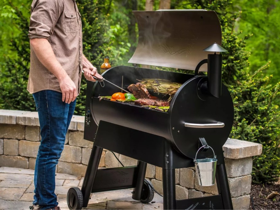 man grilling food on a large Traeger pellet grill on a back patio