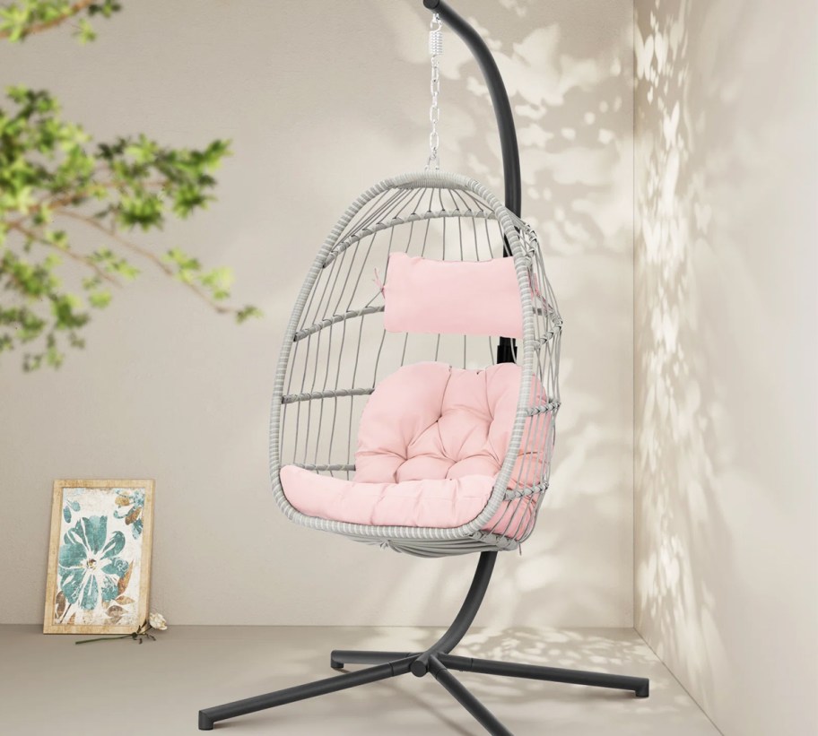 light grey hanging patio chair on stand with pink cushions