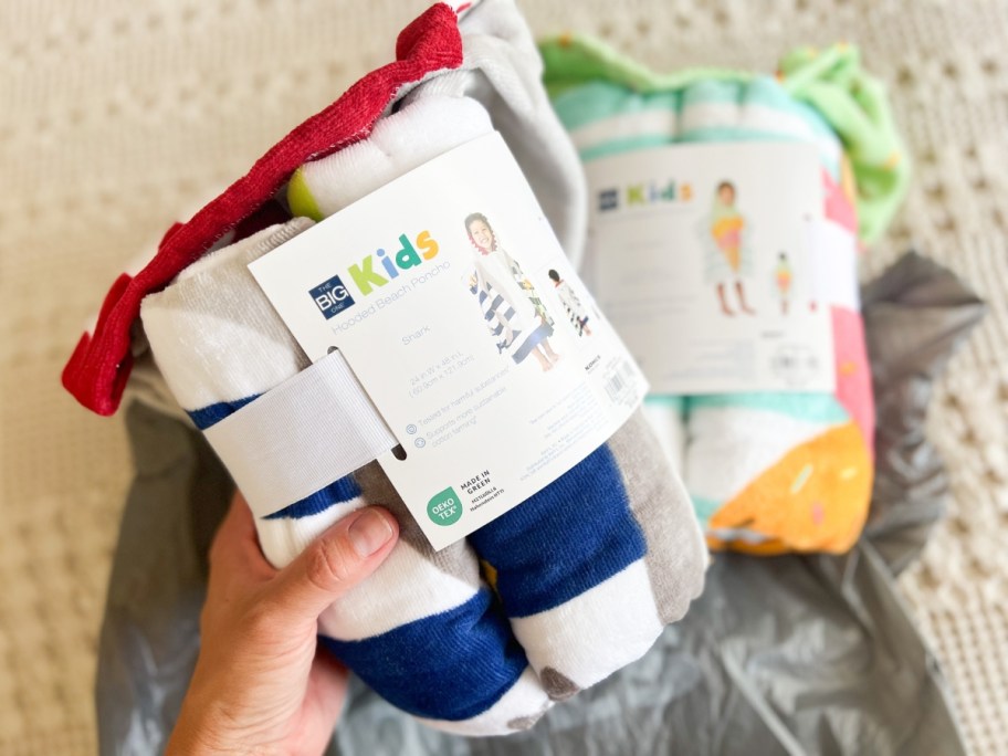 hand holding a Kid's Hooded Beach Towel in the packaging, with another laying behind it