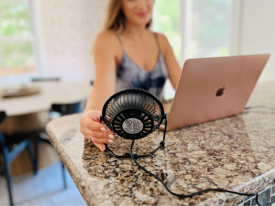 A woman working on a computer is being cooled down by a 4" personal fan.