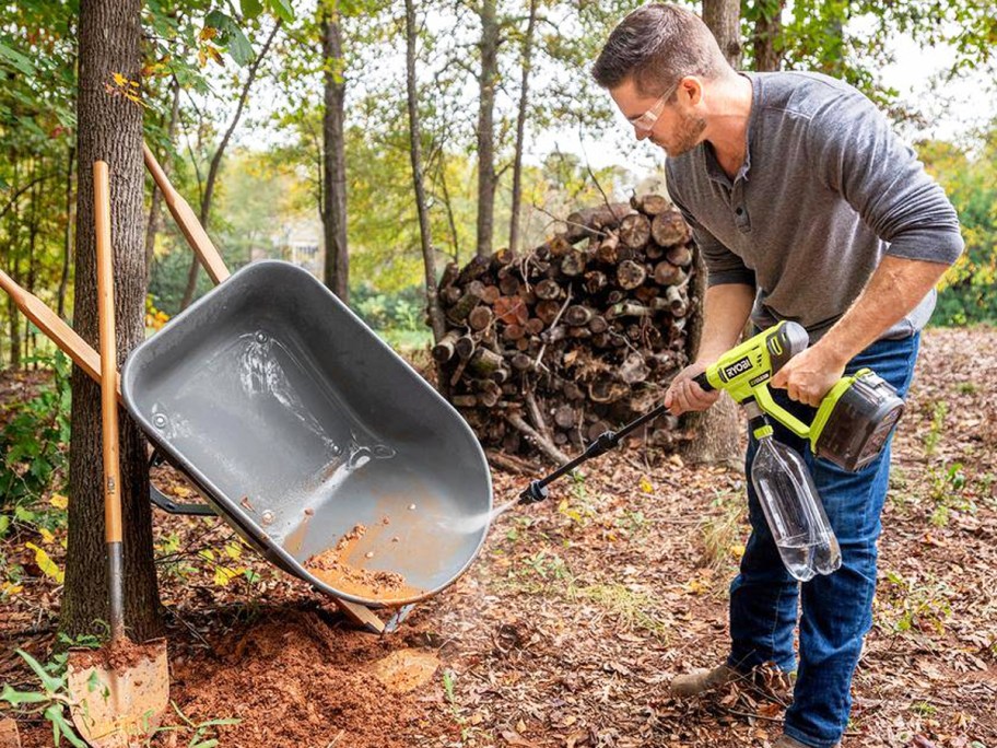 person using a yellow Ryobi pressure washer to clean a wheelbarrow