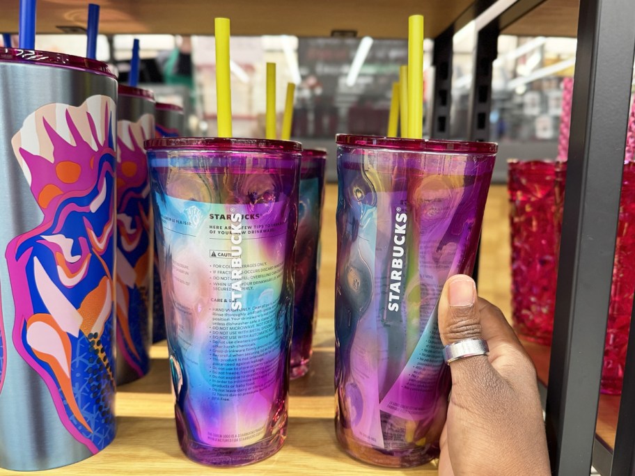 hand touching two blue/pink/purple iridescent glass starbucks tumblers on shelf