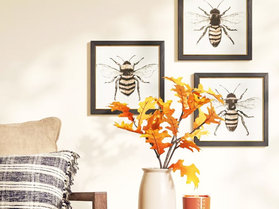 3 frames bee prints on wall behind vase of leaves