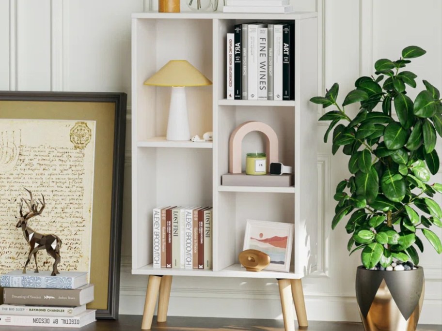 white mid century modern style small bookcase with lighter color legs filled with books and knick knacks