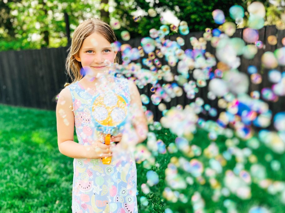 girl standing in yard shooting bubbled from a bubble blaster
