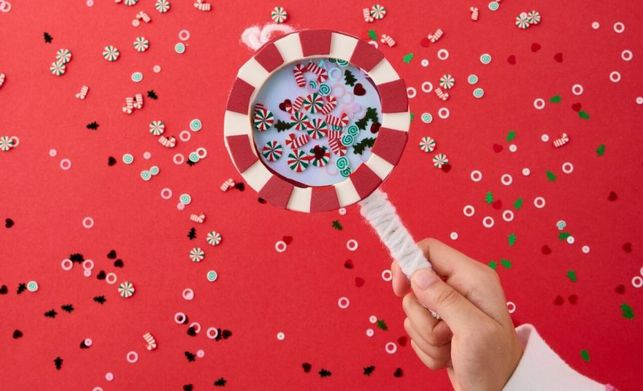 a little girls hand holding a candy cane shaker ornament craft project