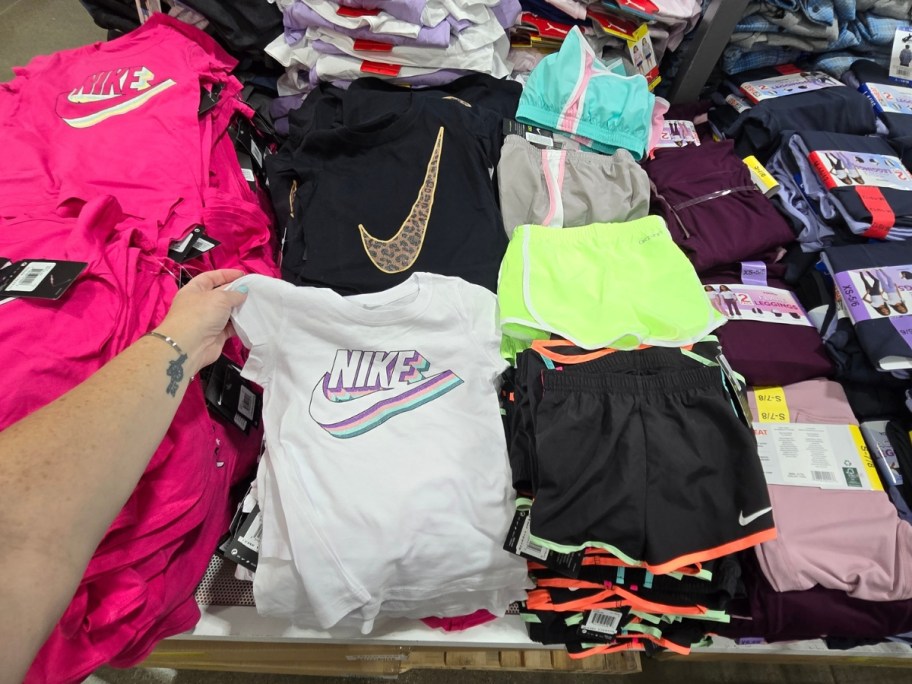 hand reaching for a kid's Nike logo tshirt on a table with more shirts in a variety of colors