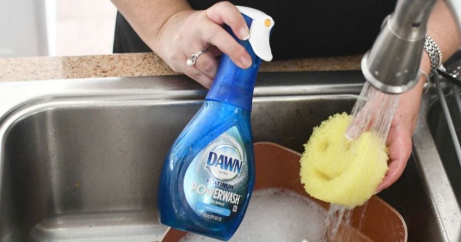 dawn powerwash bottle being held in the sink with a scrub daddy and pan with bubbles in it