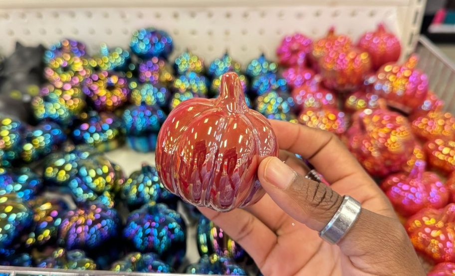 a womans hand holding up a small orange iridescent glass pumpkin