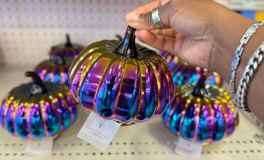 a womans hand picking up an iridescent glass pumpkin