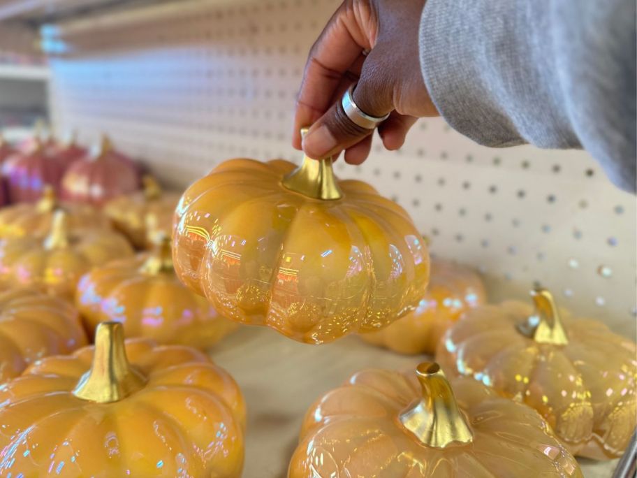 a womans hand holding up a gold iridescent glass pumpkin