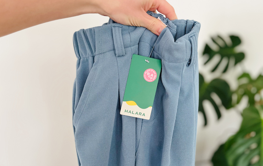 hand holding up blue halara pants in front of monstera plant