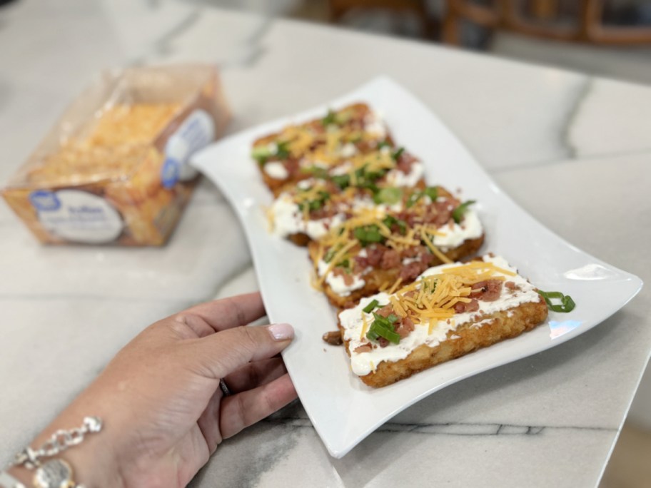 holding a plate with loaded frozen hash browns with bacon and cheese