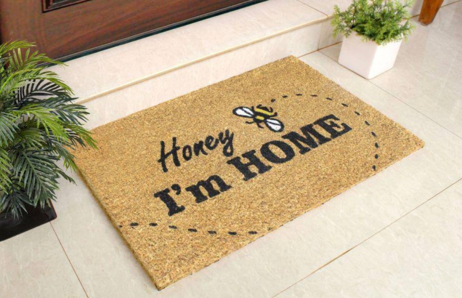 honey I'm home doormat with bee sitting at front door of house